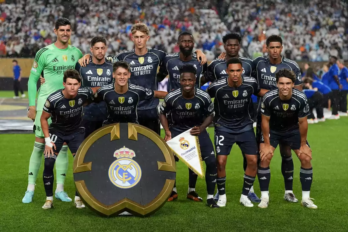 Jugadores del Real Madrid posan juntos en el campo antes de un partido con uniforme azul oscuro y un escudo grande del club al frente Jugadores del Real Madrid posan juntos en el campo antes de un partido con uniforme azul oscuro y un escudo grande del club al frente