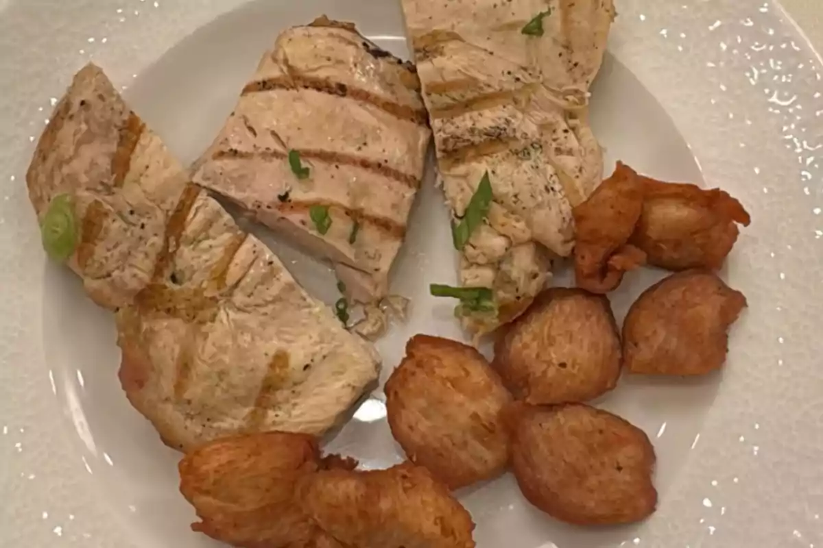 Three grilled chicken fillets served with several golden croquettes on a white plate Three grilled chicken fillets served with several golden croquettes on a white plate