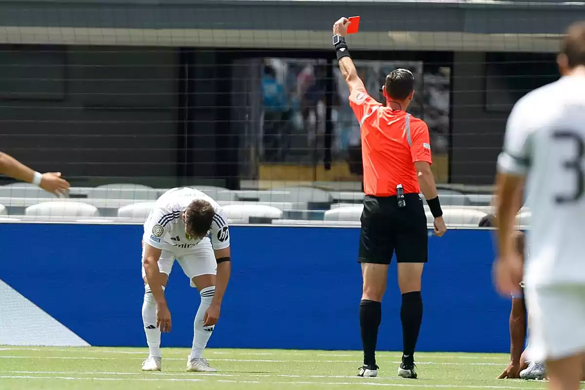 Referee showing a red card to a player who is leaning forward in frustration during a match Referee showing a red card to a player who is leaning forward in frustration during a match