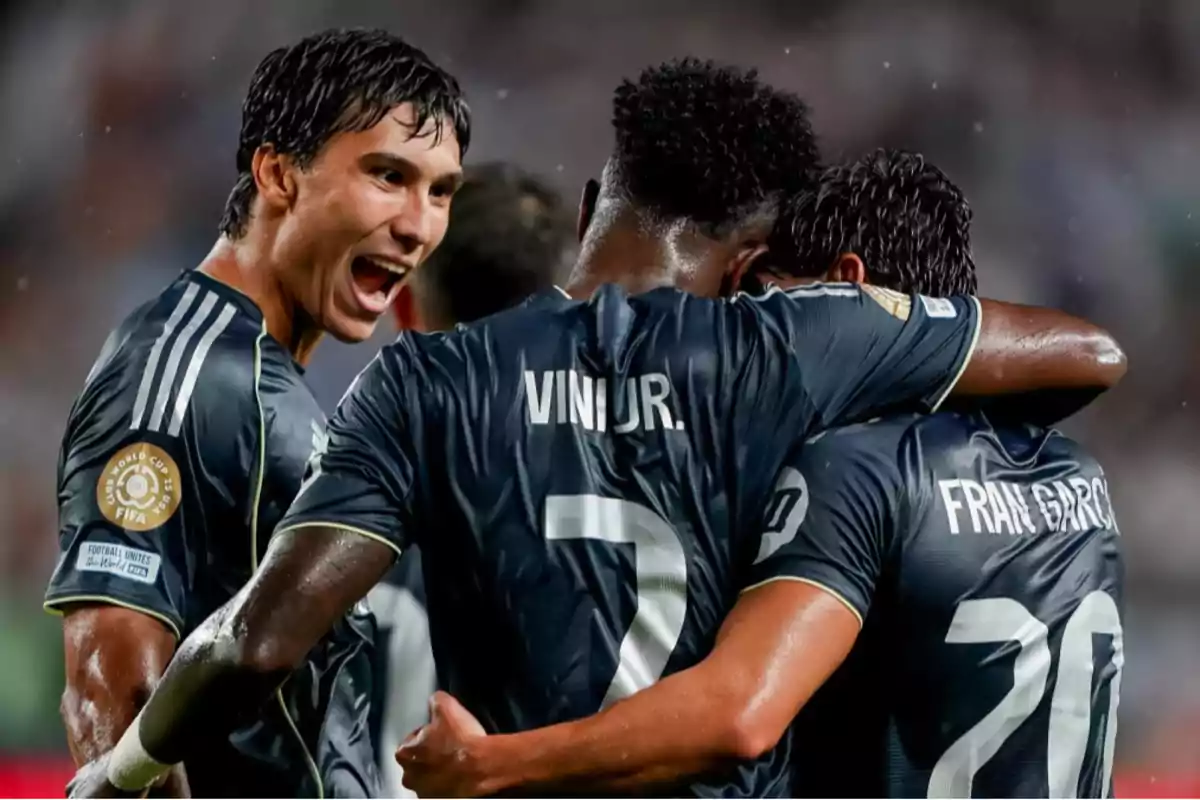 Tres futbolistas celebran un gol abrazándose en el campo mientras uno de ellos sonríe emocionado Tres futbolistas celebran un gol abrazándose en el campo mientras uno de ellos sonríe emocionado