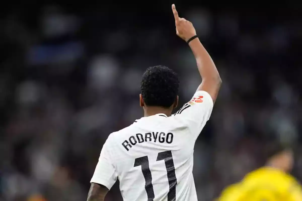 Soccer player wearing the white number 11 jersey with the name Rodrygo, raising one arm and pointing upward in a stadium Soccer player wearing the white number 11 jersey with the name Rodrygo, raising one arm and pointing upward in a stadium