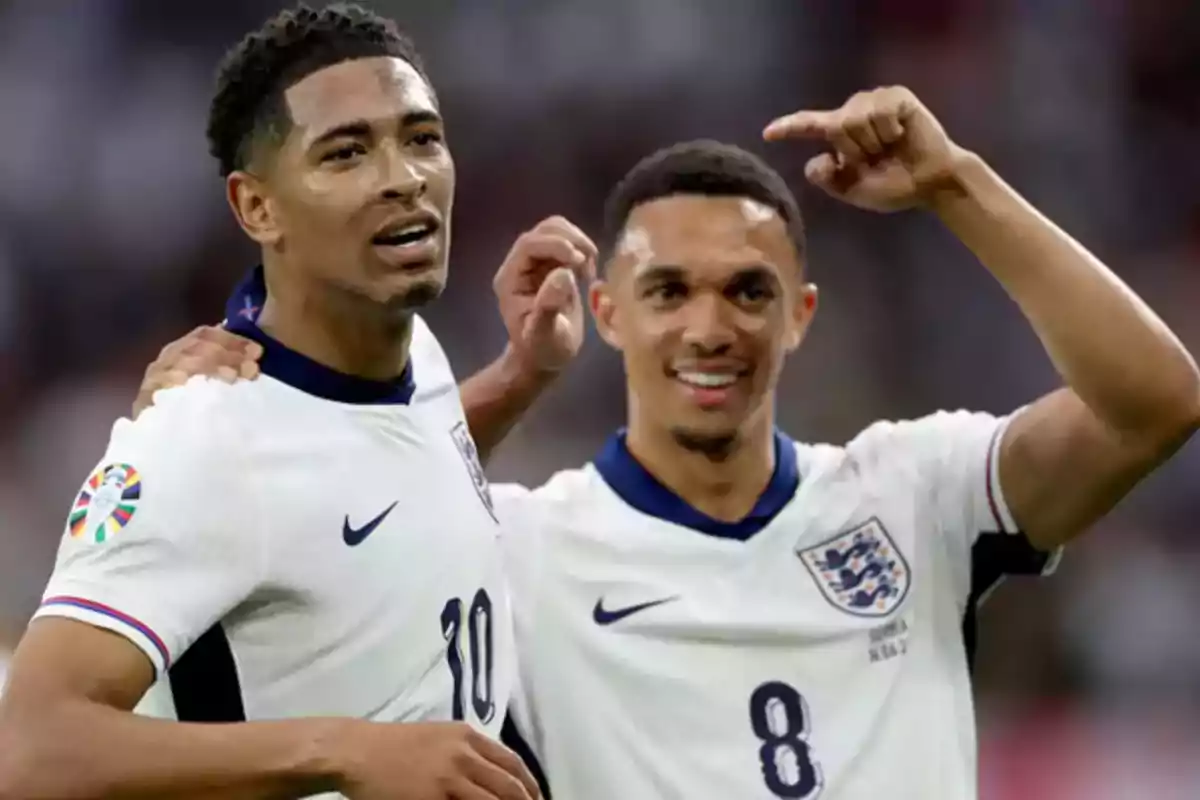 Two players from the England national team celebrate together on the field during a match, both wearing the team's white uniform. Two players from the England national team celebrate together on the field during a match, both wearing the team's white uniform.