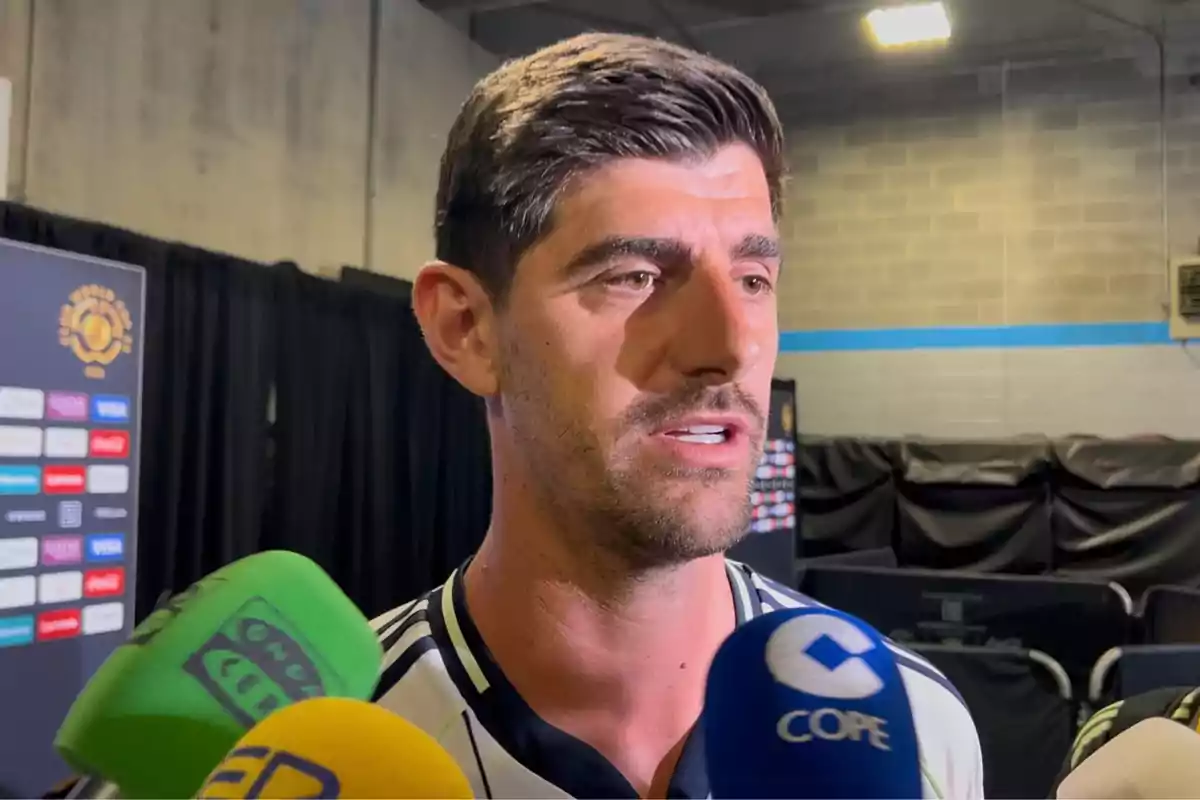 Un futbolista da una entrevista rodeado de varios micrófonos de diferentes medios en una zona mixta