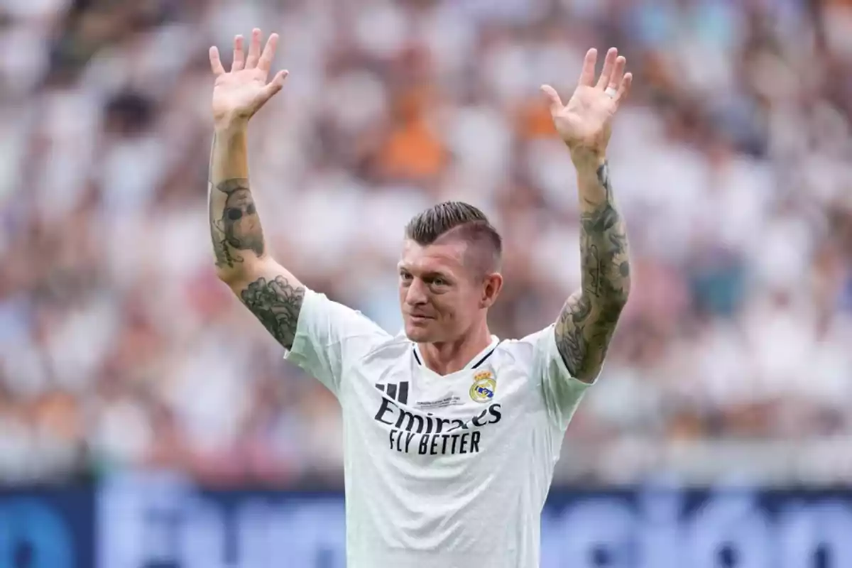 Futbolista con camiseta blanca del Real Madrid levantando ambos brazos en un estadio lleno de aficionados