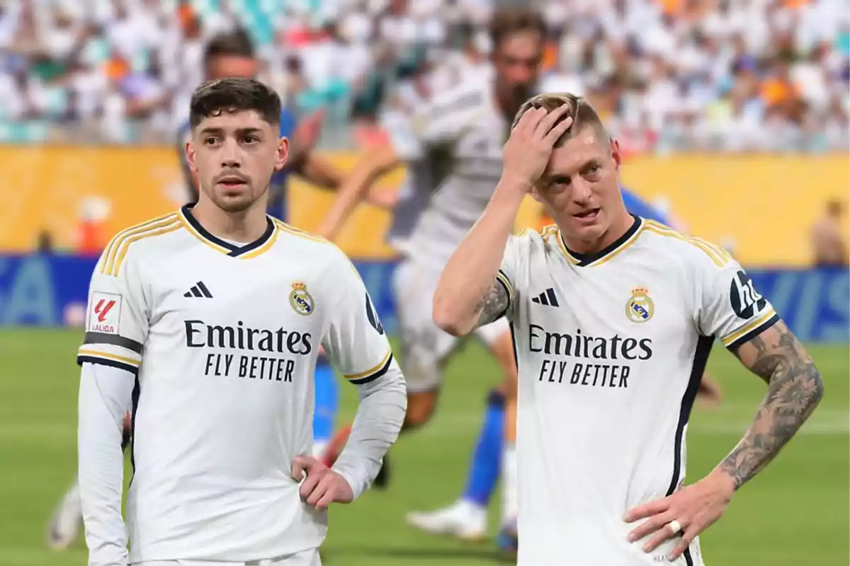 Dos futbolistas del Real Madrid con uniforme blanco en el campo durante un partido, uno de ellos se toca la cabeza y ambos lucen serios