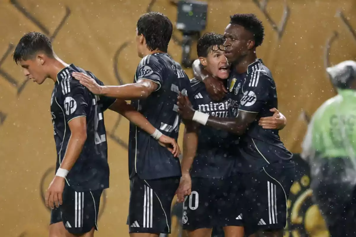 Jugadores de fútbol celebran un gol bajo la lluvia durante un partido, vistiendo uniformes oscuros y abrazándose emocionados. Jugadores de fútbol celebran un gol bajo la lluvia durante un partido, vistiendo uniformes oscuros y abrazándose emocionados.