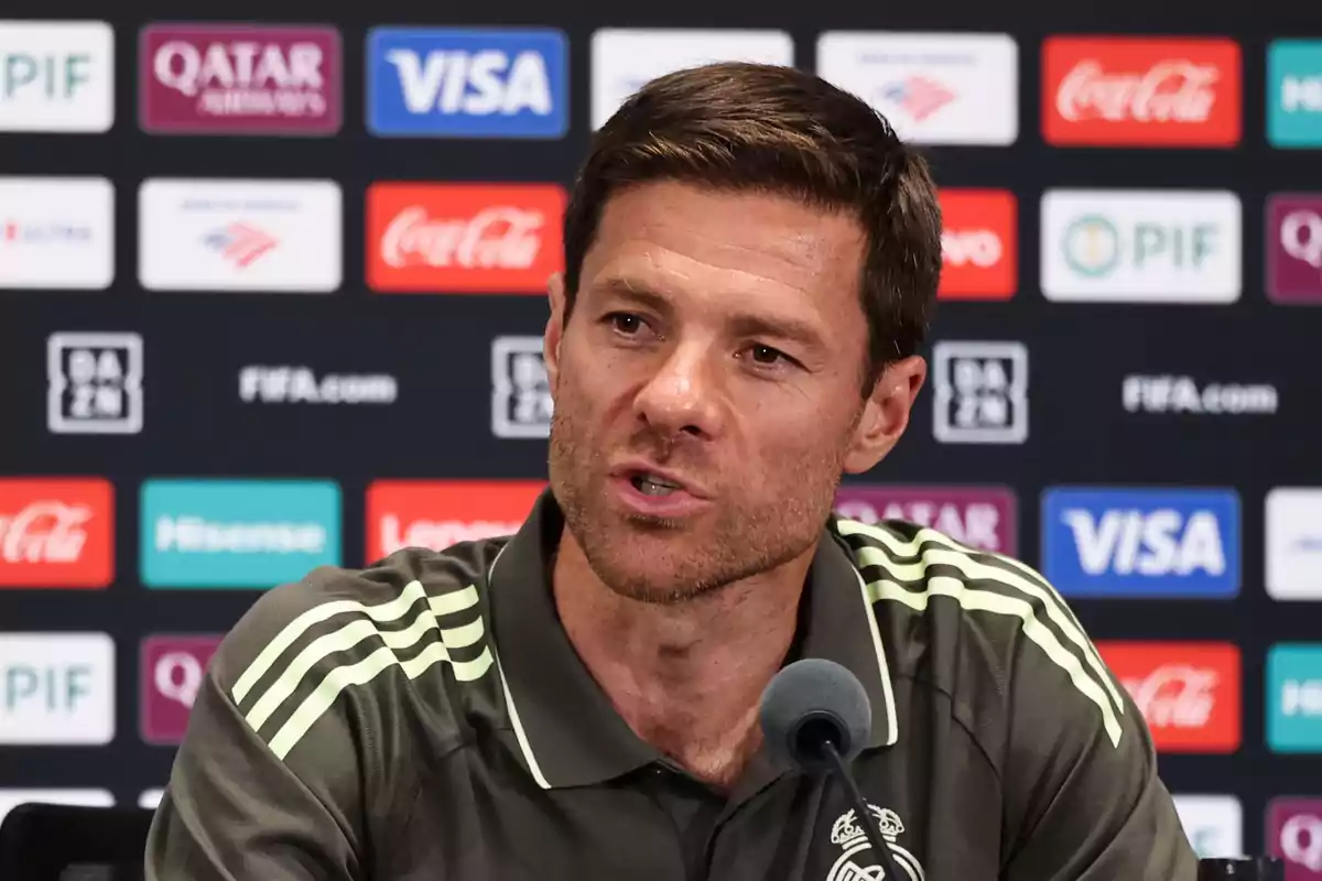 Man in a sports jersey speaking at a press conference with a backdrop of sponsor logos. Man in a sports jersey speaking at a press conference with a backdrop of sponsor logos.