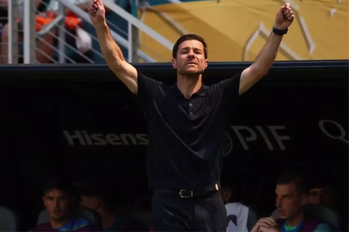 Entrenador de fútbol levantando ambos brazos en señal de celebración frente al banquillo durante un partido