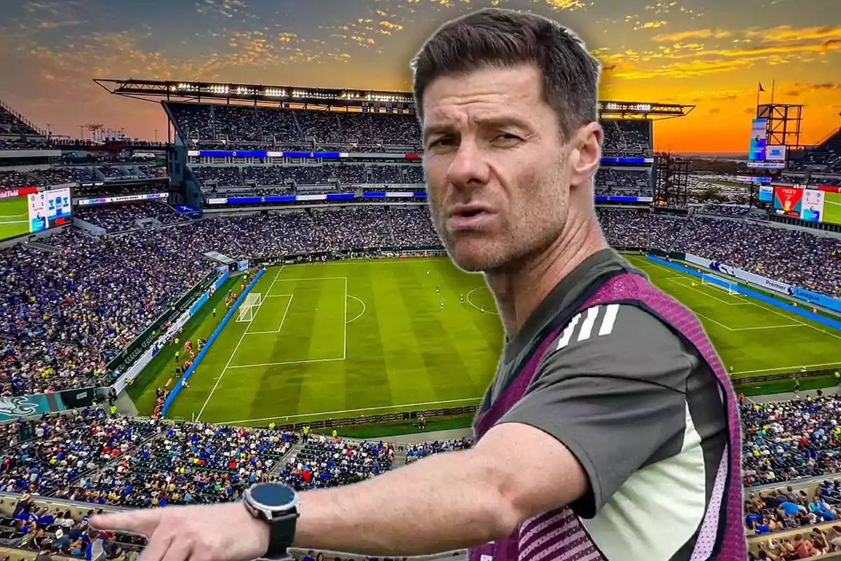 Soccer coach pointing while a stadium full of fans can be seen in the background during sunset.