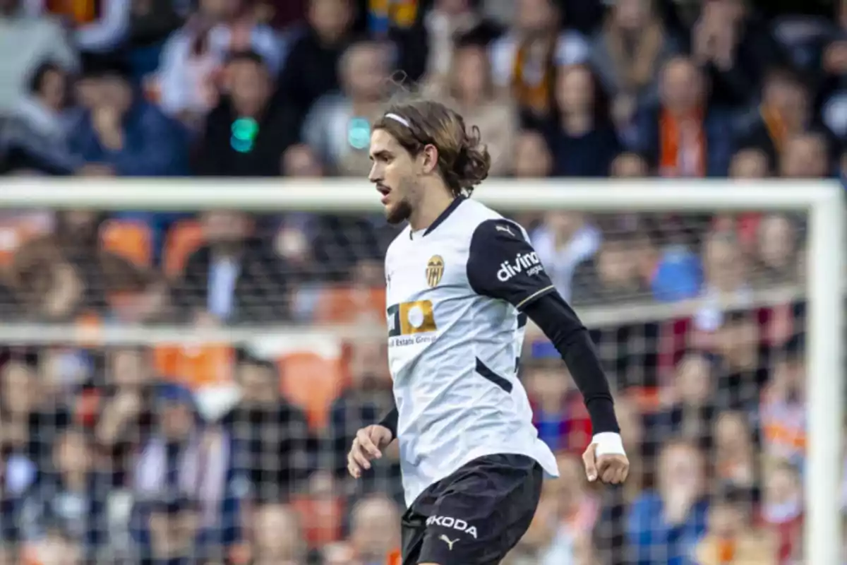 Futbolista del Valencia CF corriendo en el campo durante un partido con público en las gradas