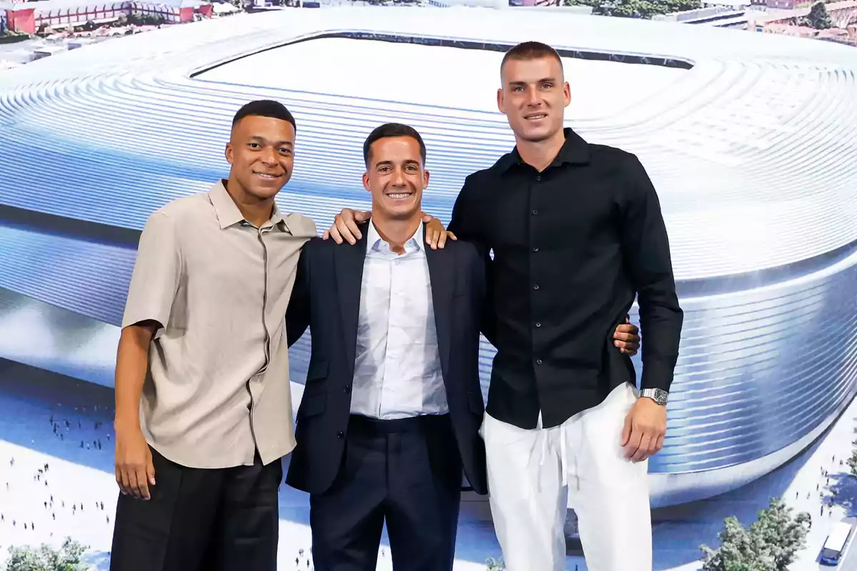 Tres hombres posan sonrientes frente a una imagen de un estadio moderno Tres hombres posan sonrientes frente a una imagen de un estadio moderno