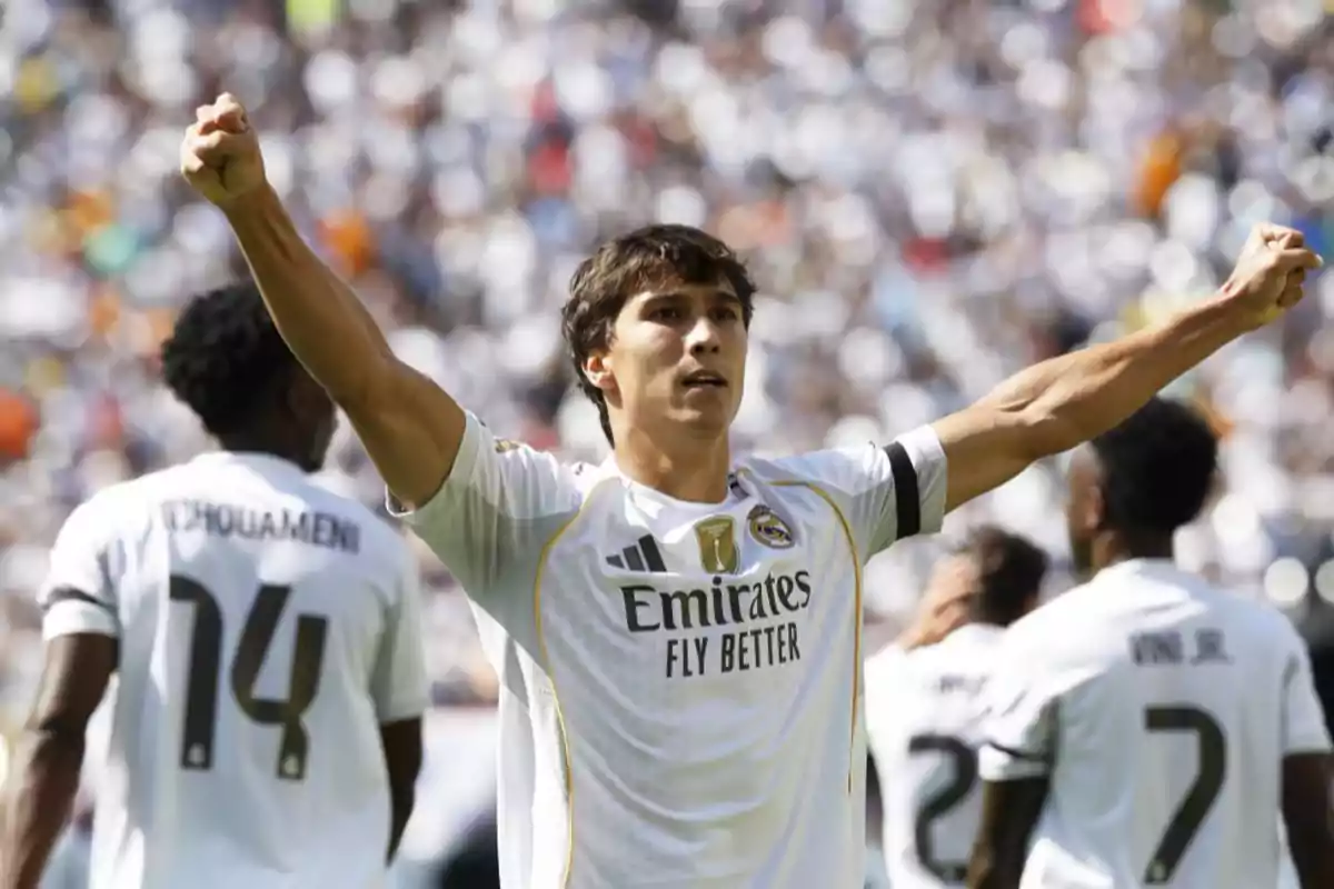 Real Madrid player celebrating a goal with arms raised during a match, surrounded by teammates and with the crowd in the background