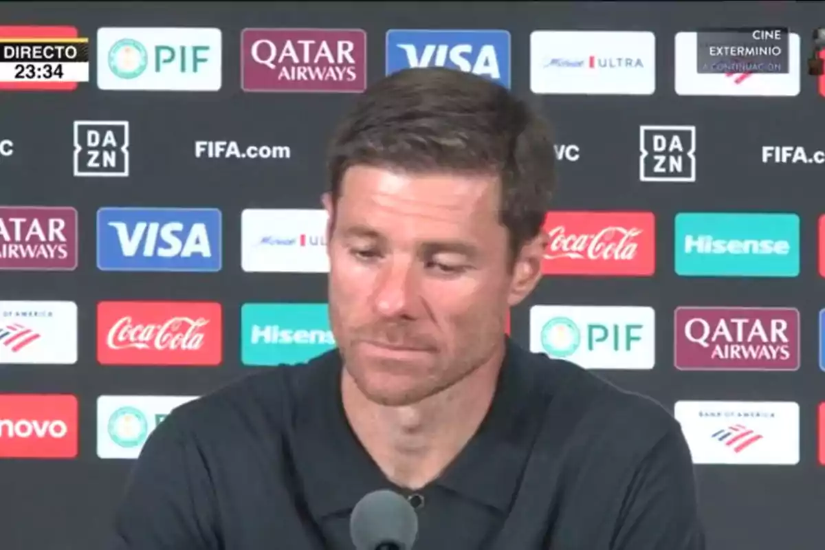 Man in a black jersey at a press conference with a backdrop of sports sponsors Man in a black jersey at a press conference with a backdrop of sports sponsors