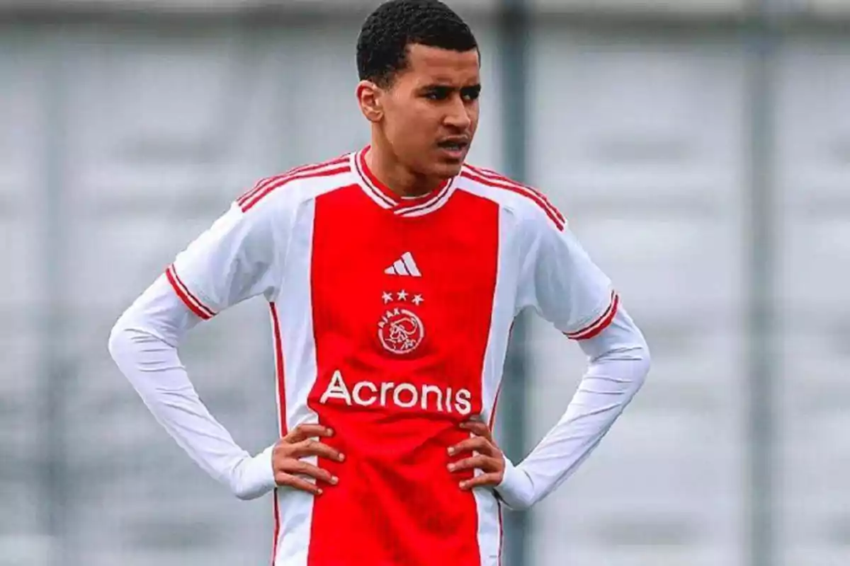 Joven futbolista con uniforme del Ajax de Ámsterdam durante un partido, con las manos en la cintura y expresión seria Joven futbolista con uniforme del Ajax de Ámsterdam durante un partido, con las manos en la cintura y expresión seria