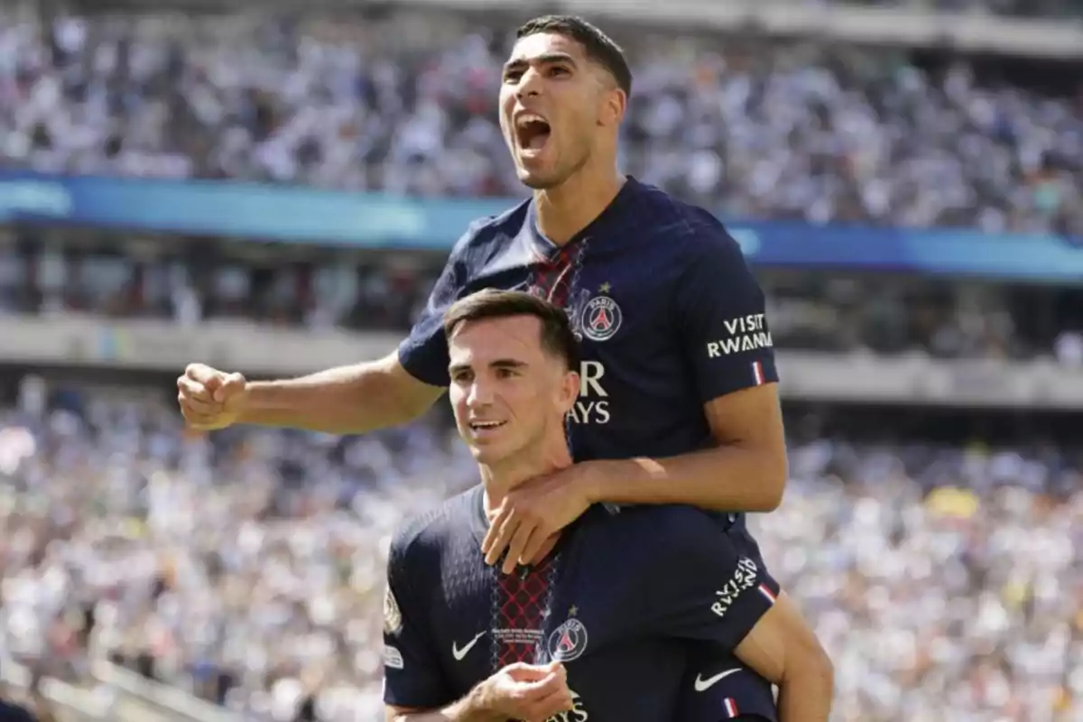 Two PSG players celebrate a goal in the stadium; one of them is on the other's shoulders and both look excited. Two PSG players celebrate a goal in the stadium; one of them is on the other's shoulders and both look excited.