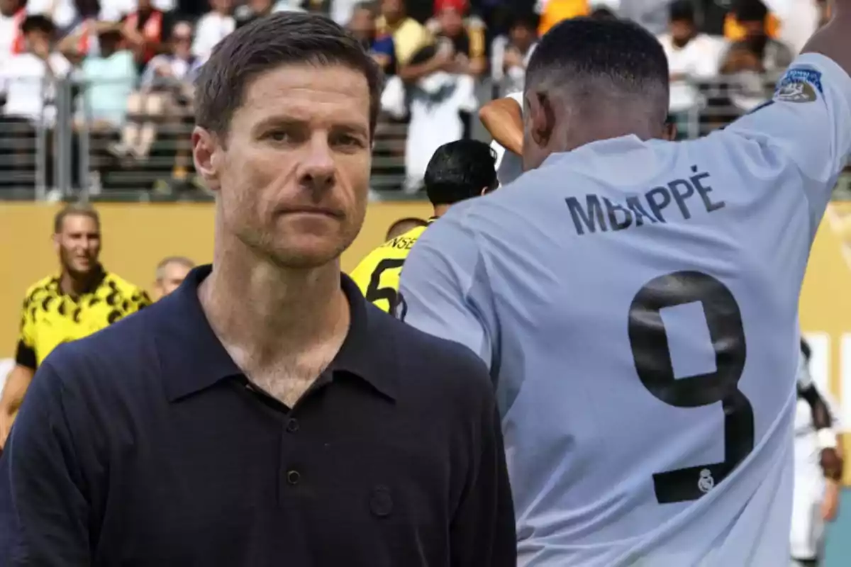 Un hombre con camisa oscura al frente y un jugador de fútbol con el nombre Mbappé y el número 9 en la camiseta blanca celebrando en un estadio lleno de público.