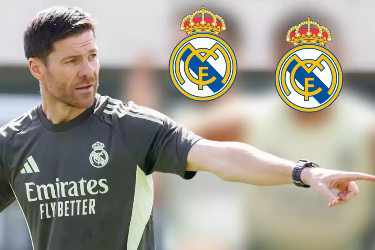 Entrenador del Real Madrid señalando con el brazo extendido mientras lleva puesta la camiseta del club y aparecen dos escudos del Real Madrid en el fondo desenfocado