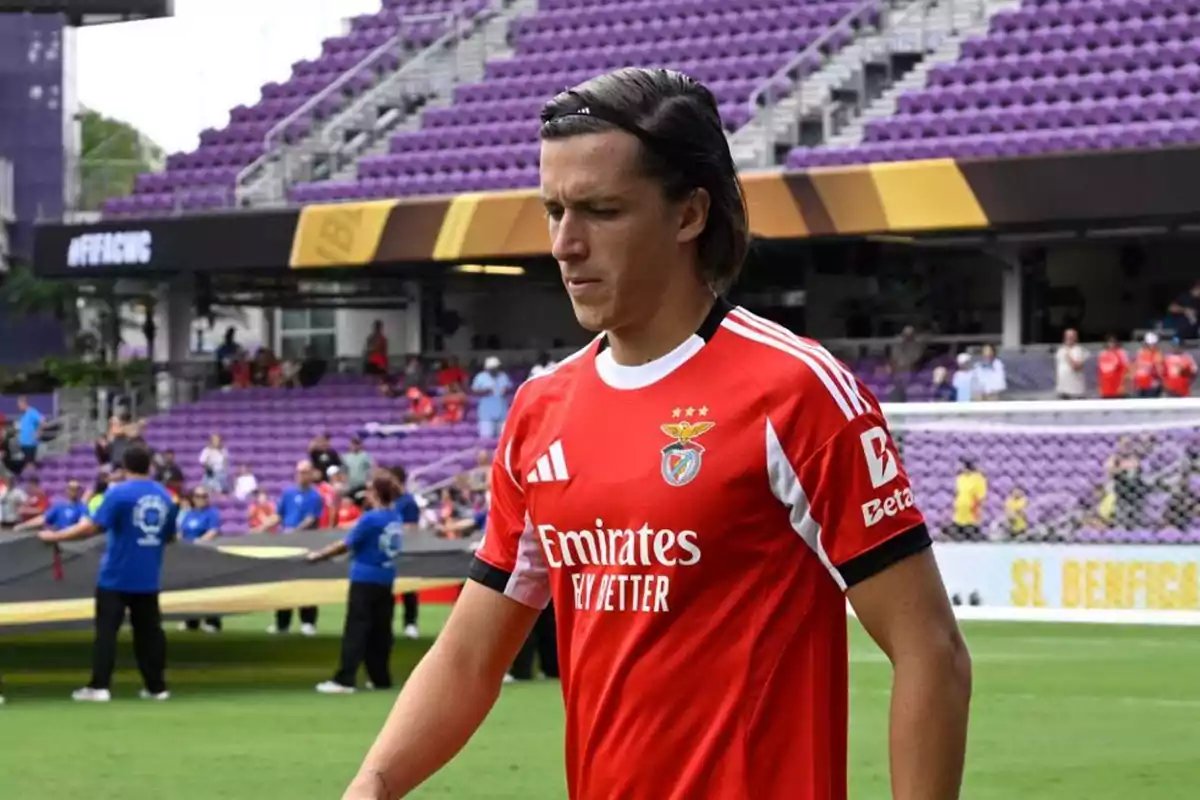 Futbolista con camiseta roja del Benfica en un estadio con gradas moradas y personas al fondo