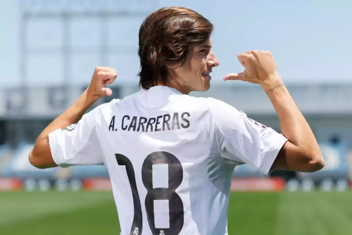 Futbolista de espaldas señalando su camiseta blanca con el nombre A. Carreras y el número 18 en un estadio al aire libre Futbolista de espaldas señalando su camiseta blanca con el nombre A. Carreras y el número 18 en un estadio al aire libre