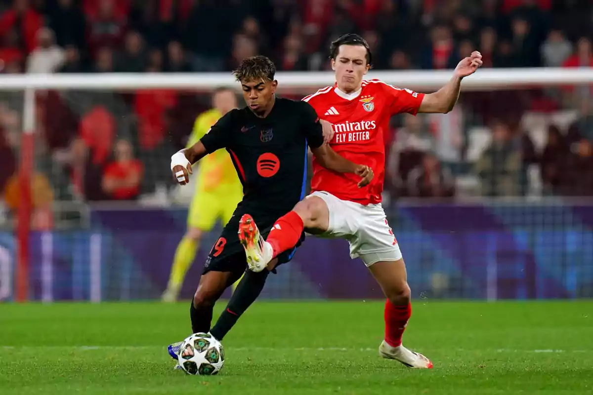 Two players compete for the ball during a match, one wearing a black uniform and the other wearing a red uniform, in a stadium full of spectators. Two players compete for the ball during a match, one wearing a black uniform and the other wearing a red uniform, in a stadium full of spectators.