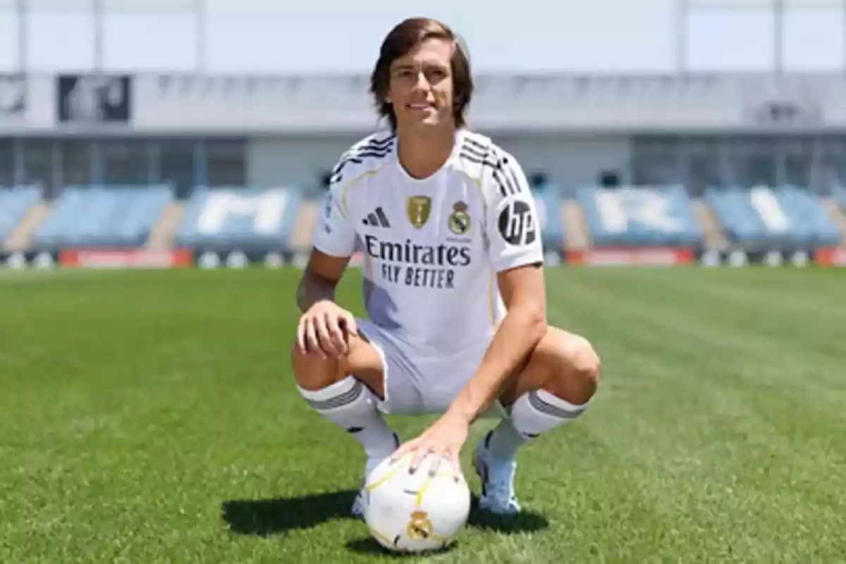 Futbolista con uniforme blanco del Real Madrid posando en una cancha de fútbol mientras sostiene un balón