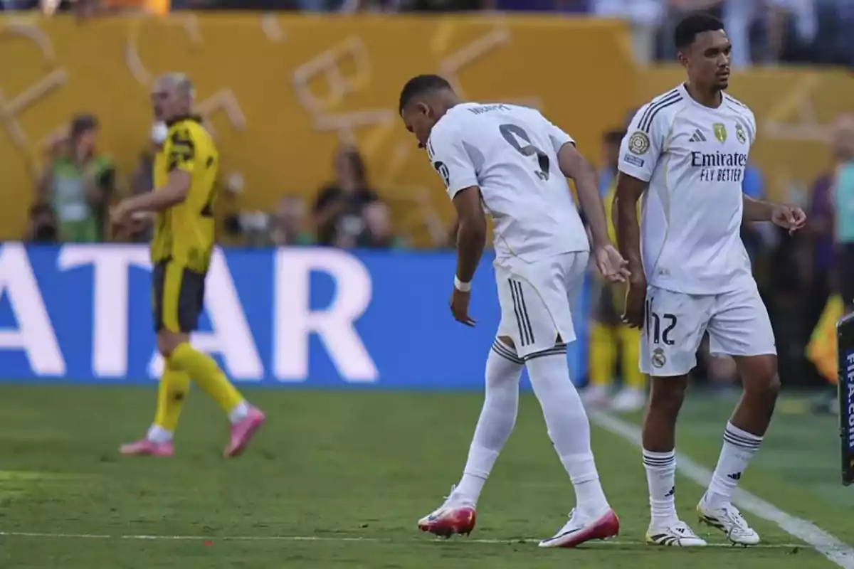 Dos jugadores del Real Madrid en uniforme blanco durante un partido de fútbol mientras un jugador del equipo rival con uniforme amarillo camina al fondo Dos jugadores del Real Madrid en uniforme blanco durante un partido de fútbol mientras un jugador del equipo rival con uniforme amarillo camina al fondo