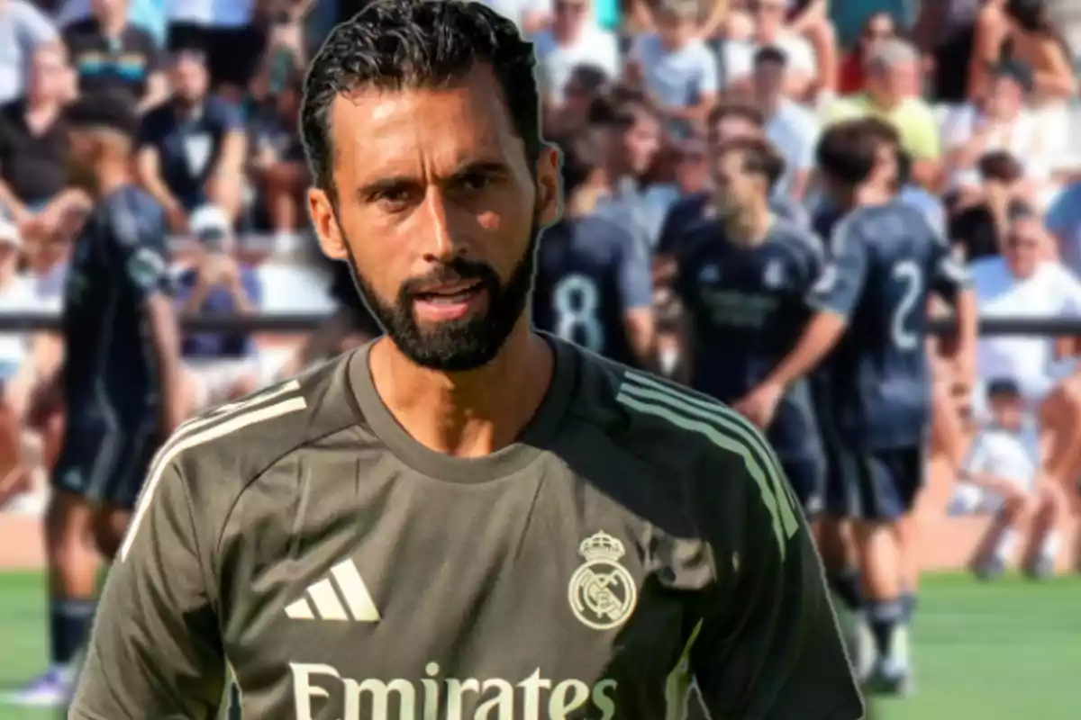 Entrenador de fútbol con camiseta del Real Madrid en un campo de entrenamiento con jugadores y público al fondo