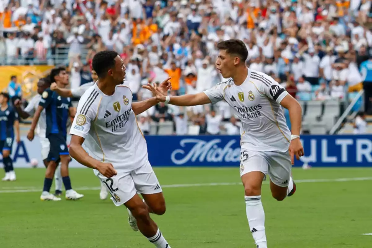 Two Real Madrid players celebrate a goal on the field while the crowd applauds in the stands. Two Real Madrid players celebrate a goal on the field while the crowd applauds in the stands.