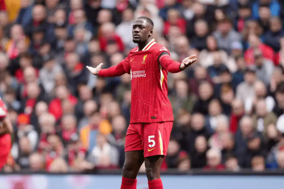 Liverpool player wearing number 5 on the red uniform raising his arms in the middle of a match with the crowd in the background