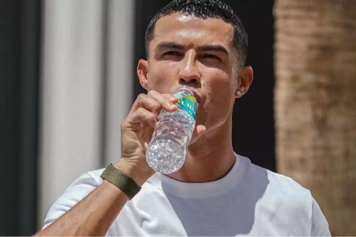 Hombre con camiseta blanca bebiendo agua de una botella de plástico al aire libre Hombre con camiseta blanca bebiendo agua de una botella de plástico al aire libre