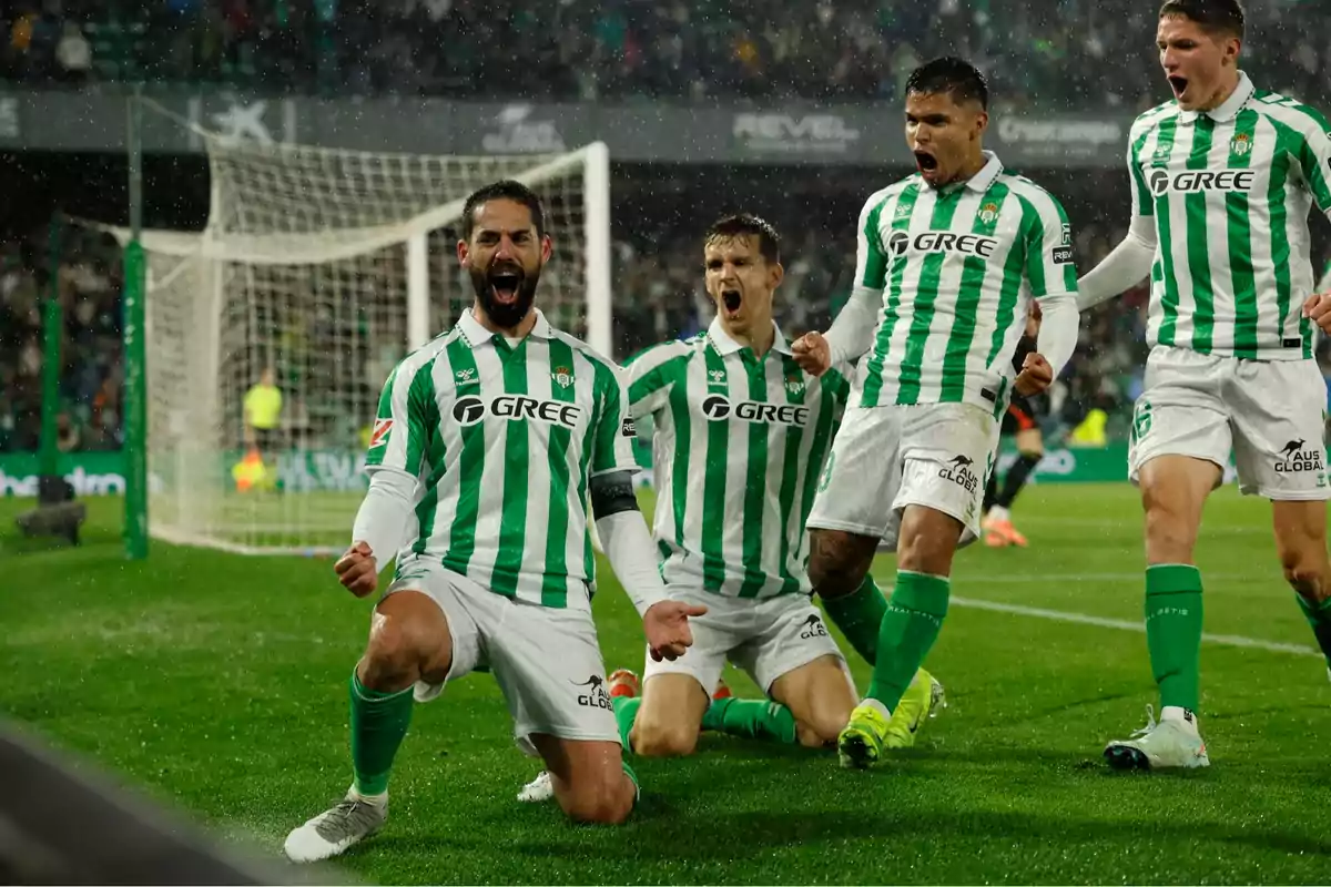 Jugadores del Real Betis celebran un gol bajo la lluvia en el estadio, mostrando emoción y energía frente a la portería Jugadores del Real Betis celebran un gol bajo la lluvia en el estadio, mostrando emoción y energía frente a la portería