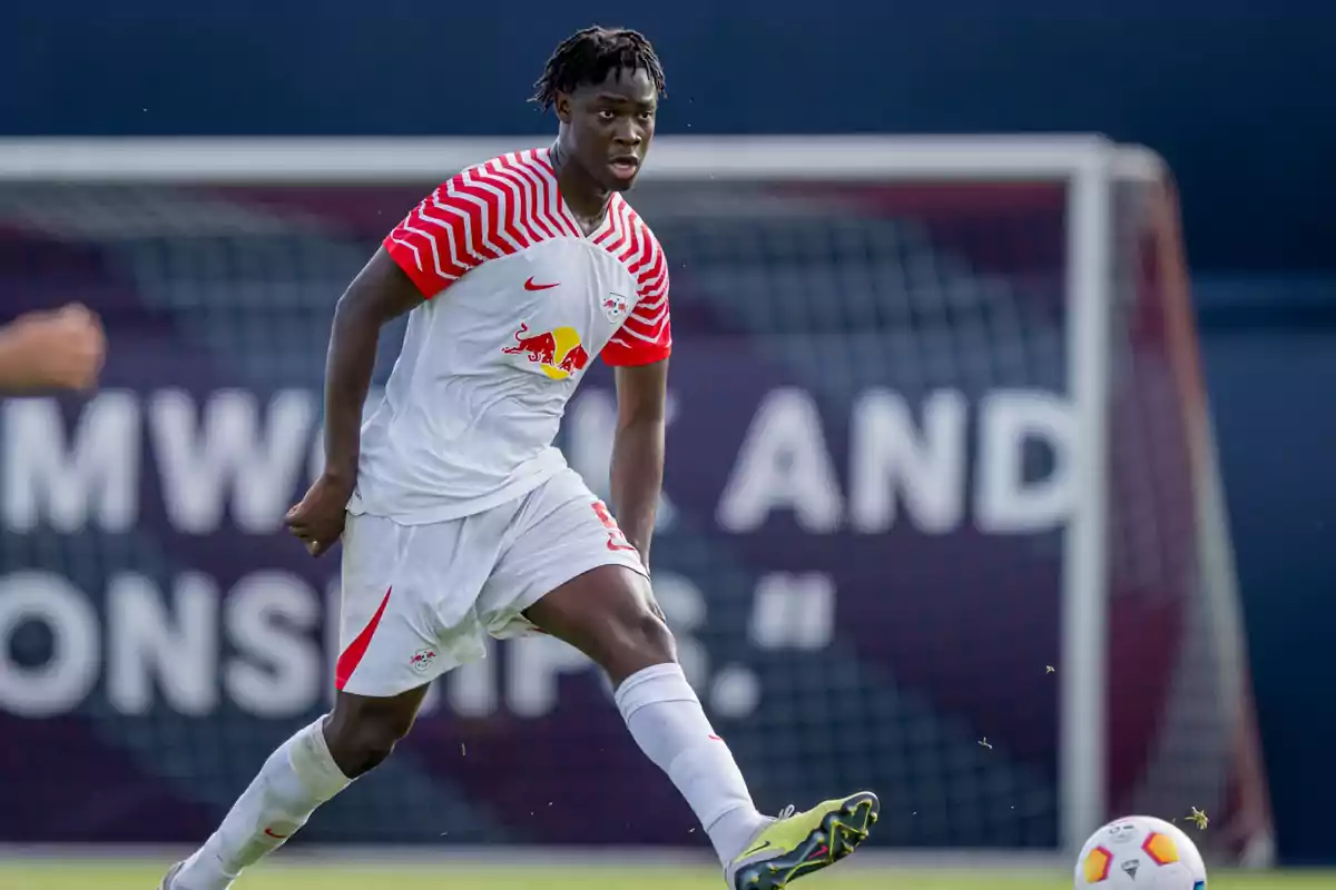 Futbolista con uniforme blanco y rojo del RB Leipzig en acción durante un partido frente a una portería.