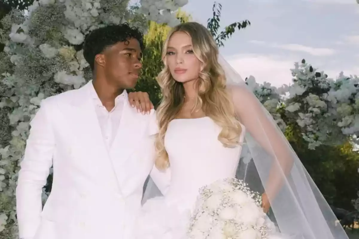 Couple dressed as bride and groom posing together at an outdoor wedding surrounded by white flowers Couple dressed as bride and groom posing together at an outdoor wedding surrounded by white flowers