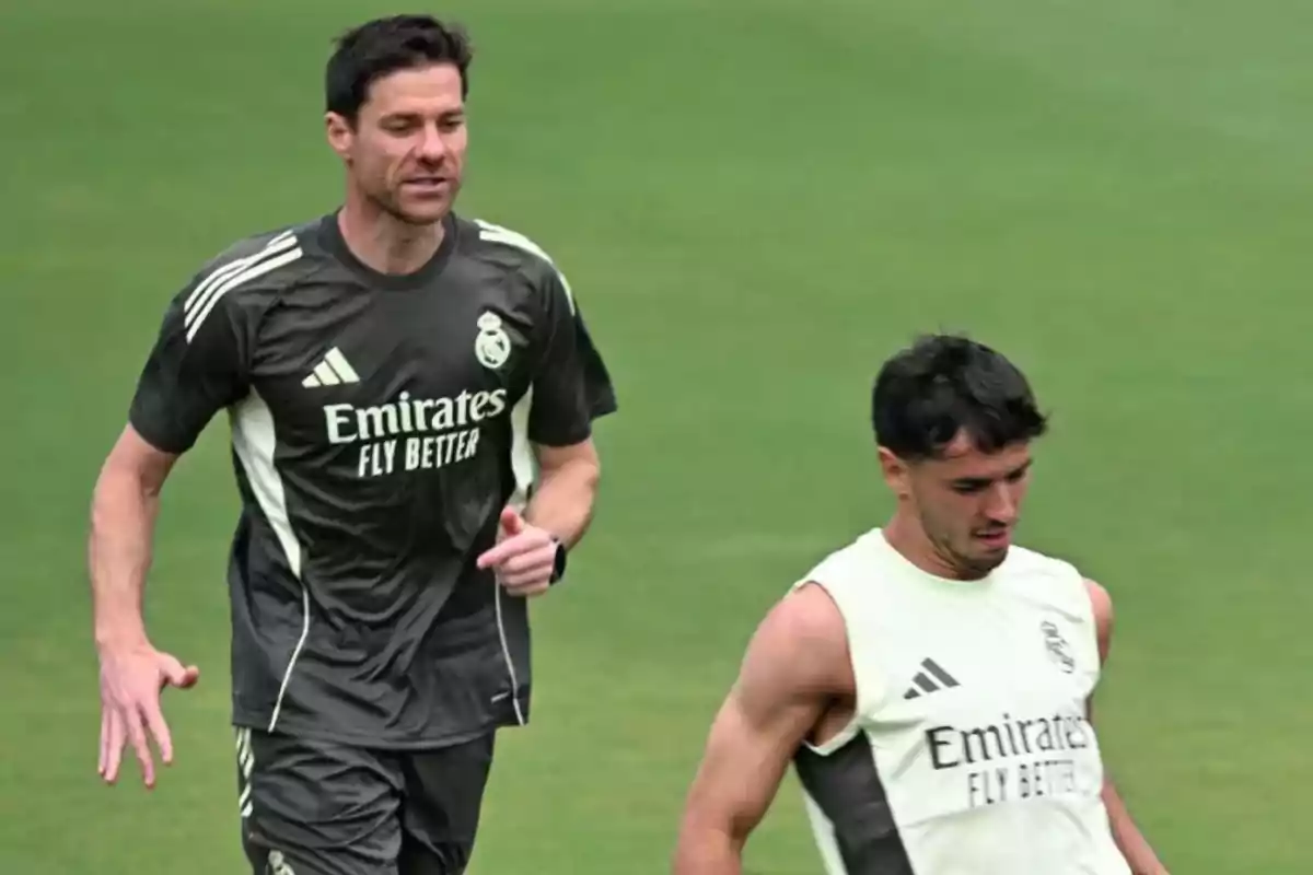 Two people wearing Real Madrid training gear run on the grass during a soccer practice. Two people wearing Real Madrid training gear run on the grass during a soccer practice.