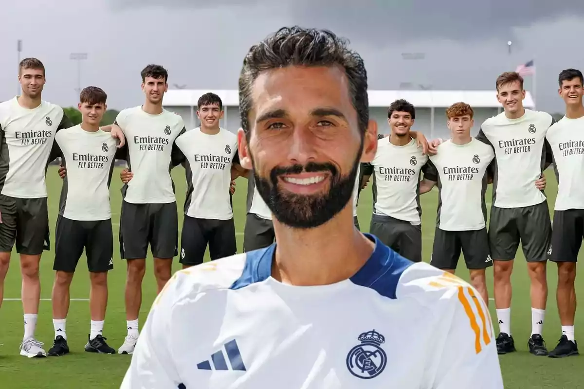 Entrenador del Real Madrid posando sonriente frente a un grupo de jóvenes futbolistas del equipo en un campo de entrenamiento