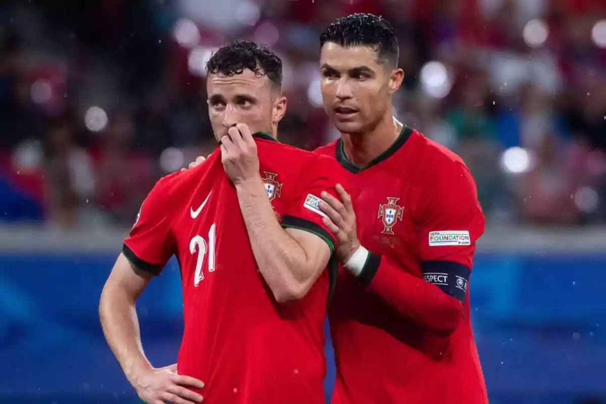 Dos futbolistas de la selección de Portugal conversan en el campo durante un partido, ambos visten uniforme rojo y uno de ellos cubre parcialmente su rostro con la camiseta. Dos futbolistas de la selección de Portugal conversan en el campo durante un partido, ambos visten uniforme rojo y uno de ellos cubre parcialmente su rostro con la camiseta.