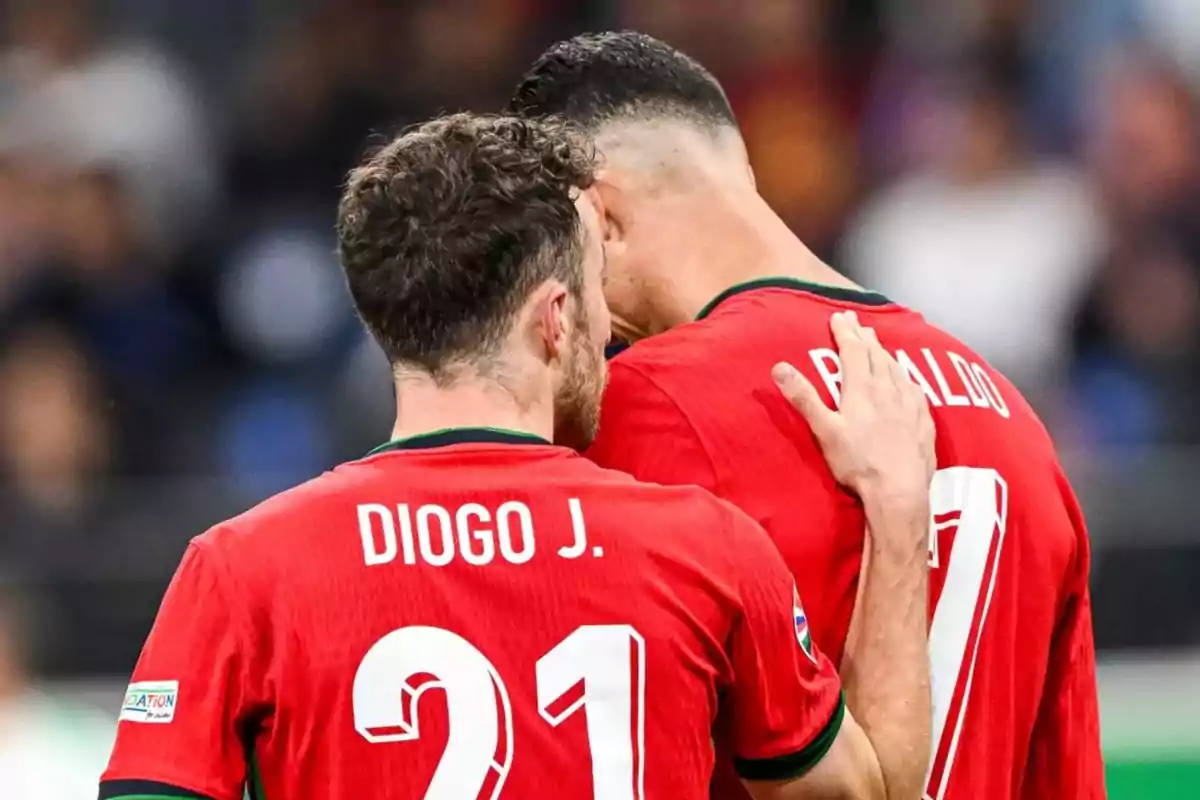 Dos futbolistas de la selección de Portugal se abrazan en el campo, uno de ellos lleva la camiseta con el nombre Diogo J y el número 21, el otro lleva la camiseta con el nombre Ronaldo y el número 7