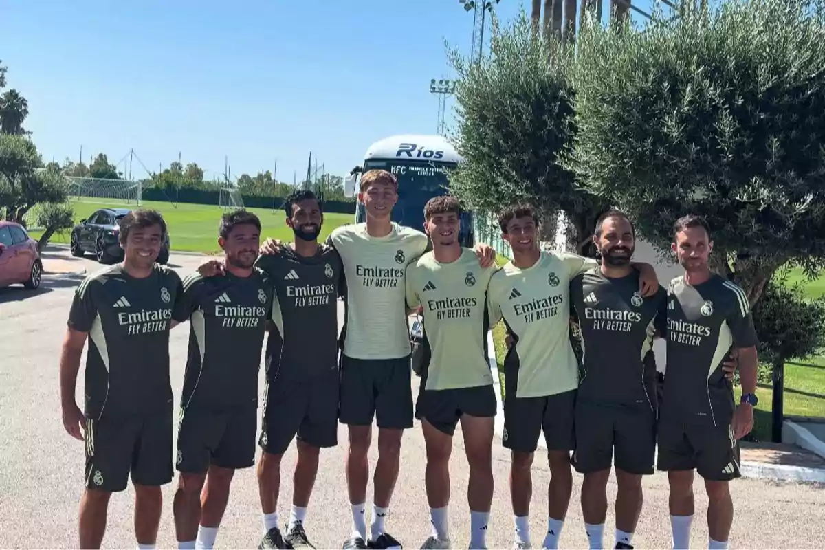 Grupo de jugadores y entrenadores del Real Madrid posando juntos al aire libre en un campo de entrenamiento con árboles y un autobús de fondo Grupo de jugadores y entrenadores del Real Madrid posando juntos al aire libre en un campo de entrenamiento con árboles y un autobús de fondo