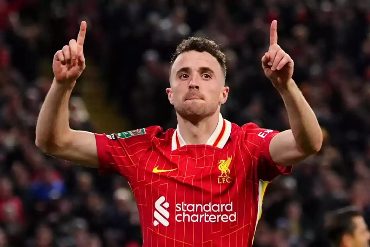 Futbolista del Liverpool celebrando un gol con ambos brazos levantados y señalando hacia arriba en un estadio lleno de aficionados Futbolista del Liverpool celebrando un gol con ambos brazos levantados y señalando hacia arriba en un estadio lleno de aficionados