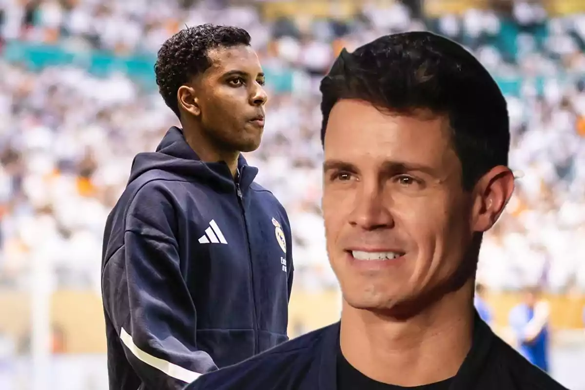 A player in a navy blue sweatjersey and a smiling man in the foreground, both in a stadium full of spectators.