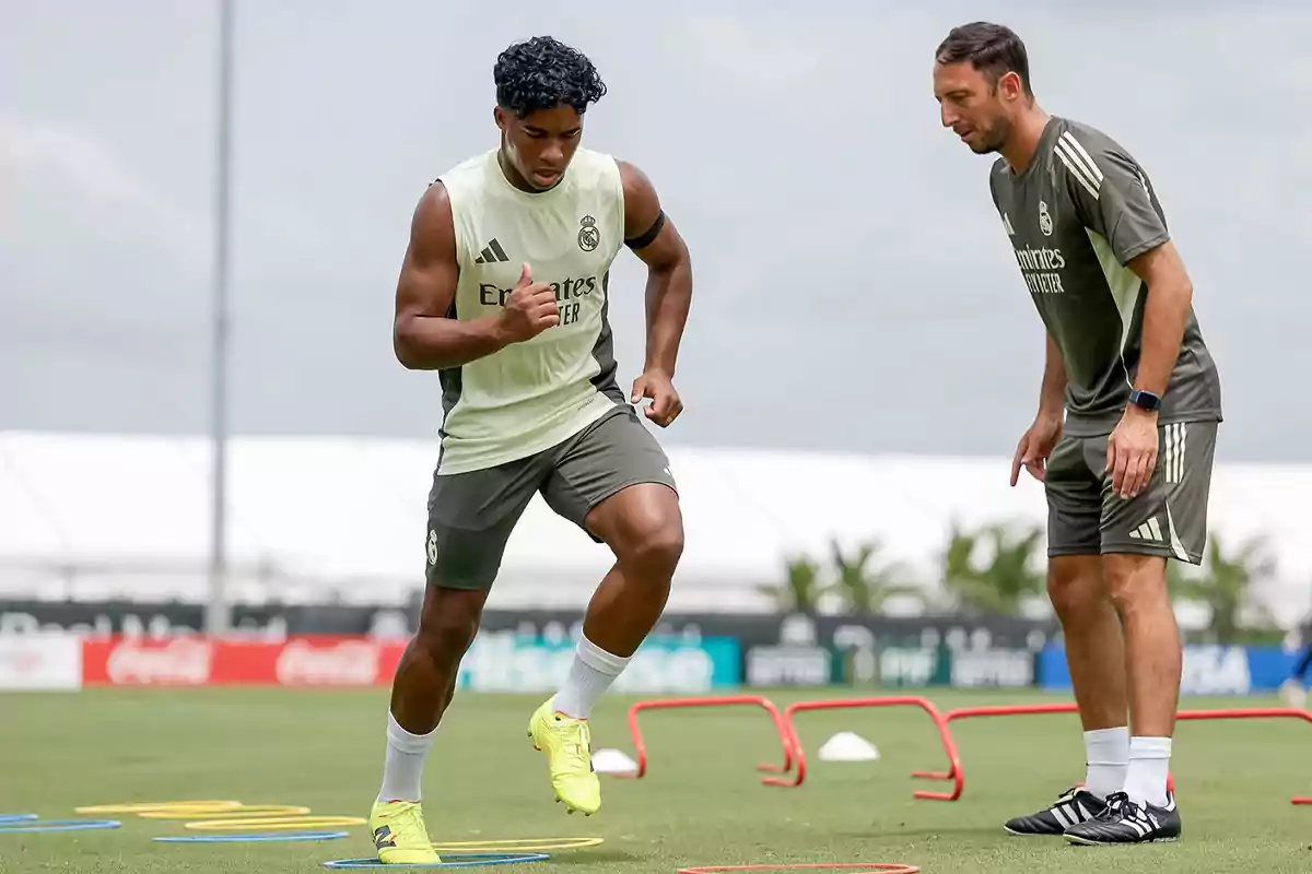 Soccer player training on the field with coach watching and agility hurdles on the ground Soccer player training on the field with coach watching and agility hurdles on the ground