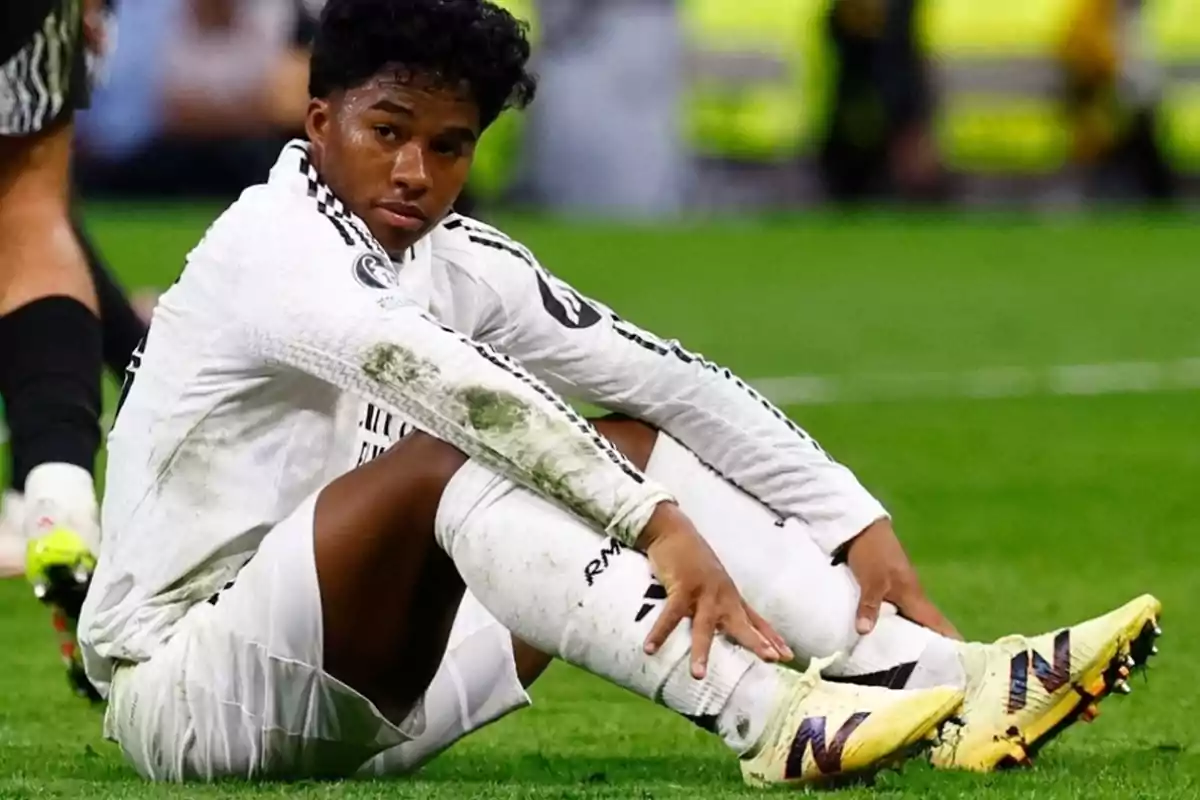Futbolista sentado en el césped con uniforme blanco y manchas de pasto en la manga y la pierna Futbolista sentado en el césped con uniforme blanco y manchas de pasto en la manga y la pierna