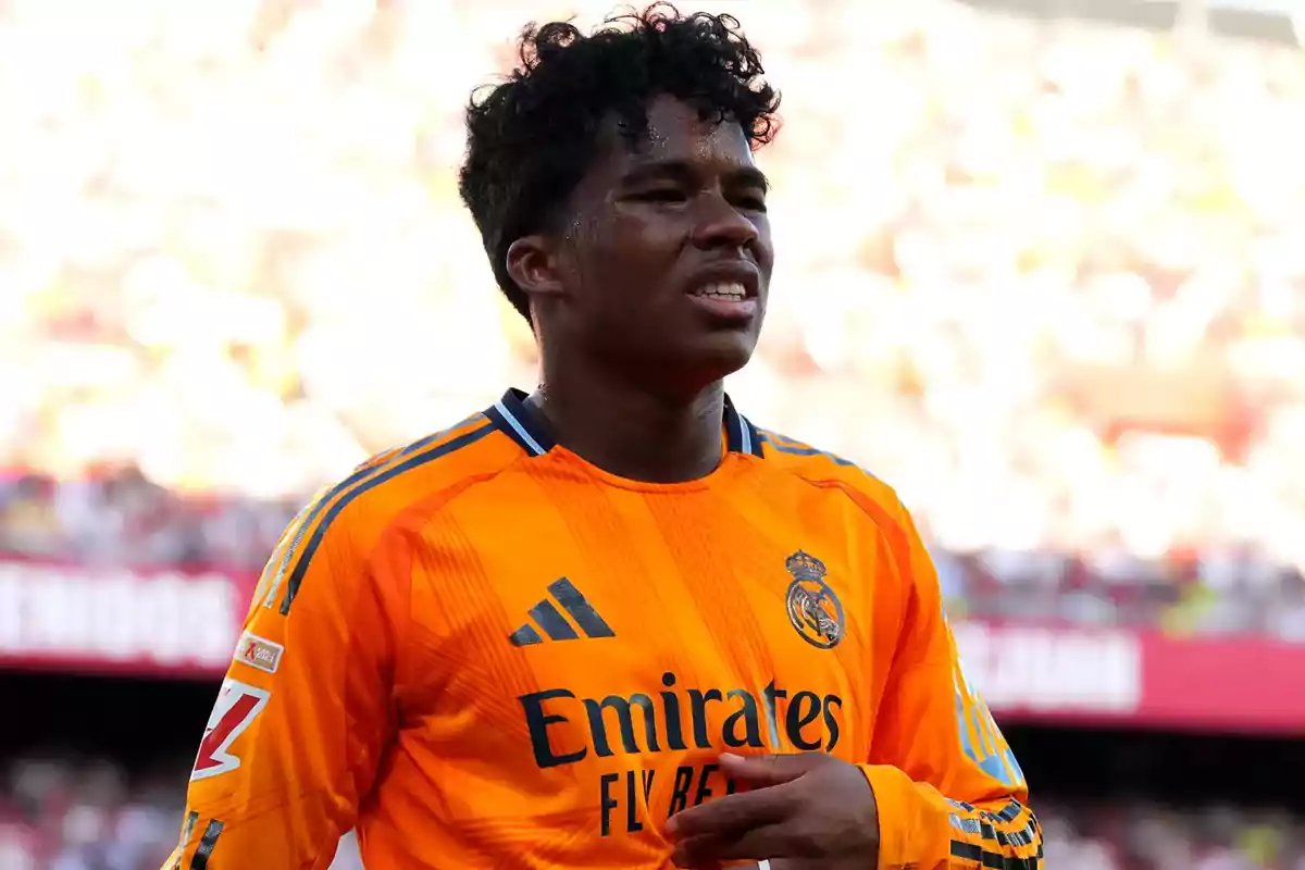 Jugador de fútbol con uniforme naranja del Real Madrid en el campo durante un partido diurno