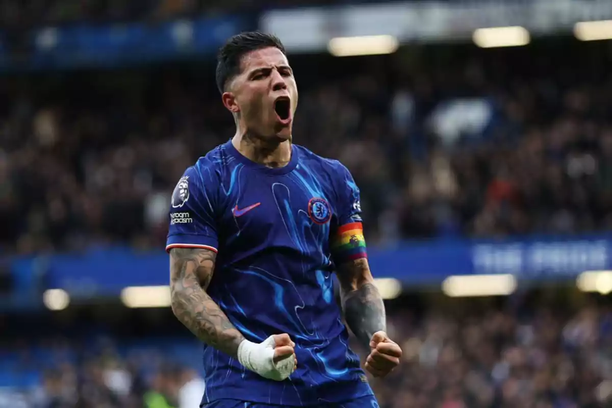 Soccer player in a blue uniform celebrating a goal with clenched fists and a rainbow captain's armband on his left arm in a stadium full of spectators. Soccer player in a blue uniform celebrating a goal with clenched fists and a rainbow captain's armband on his left arm in a stadium full of spectators.