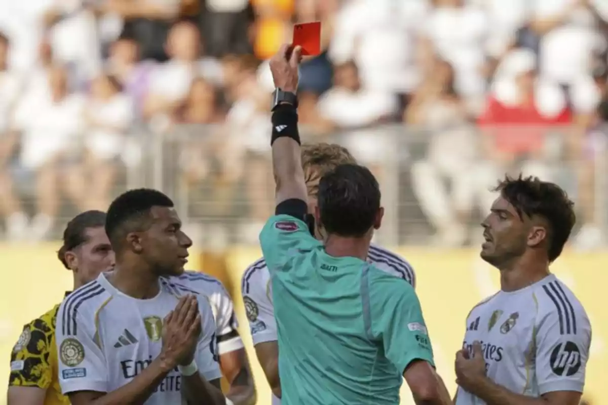 Un árbitro muestra una tarjeta roja a un jugador durante un partido de fútbol mientras otros futbolistas observan la escena