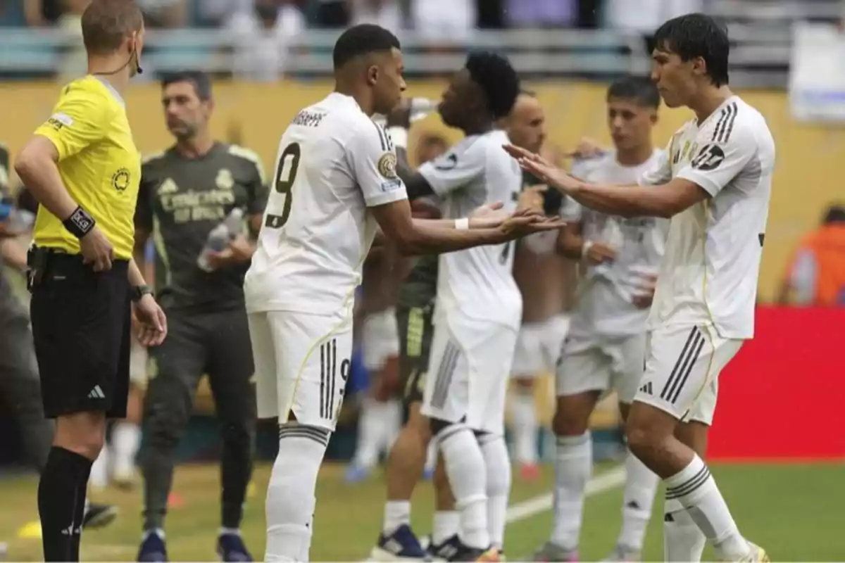 Two players in white uniforms shake hands during a substitution in a match while a referee watches and other players are in the background. Two players in white uniforms shake hands during a substitution in a match while a referee watches and other players are in the background.