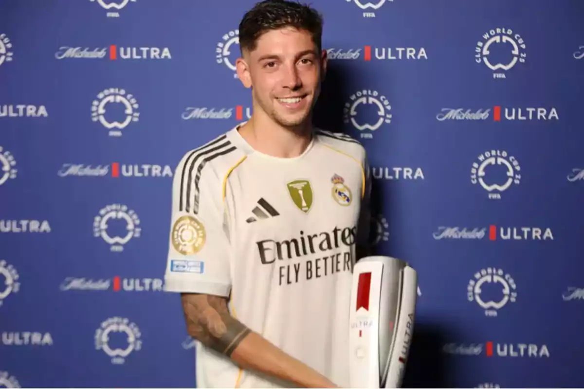 Jugador del Real Madrid sonríe mientras sostiene un trofeo frente a un fondo azul con logotipos de la Copa Mundial de Clubes y Michelob Ultra Jugador del Real Madrid sonríe mientras sostiene un trofeo frente a un fondo azul con logotipos de la Copa Mundial de Clubes y Michelob Ultra