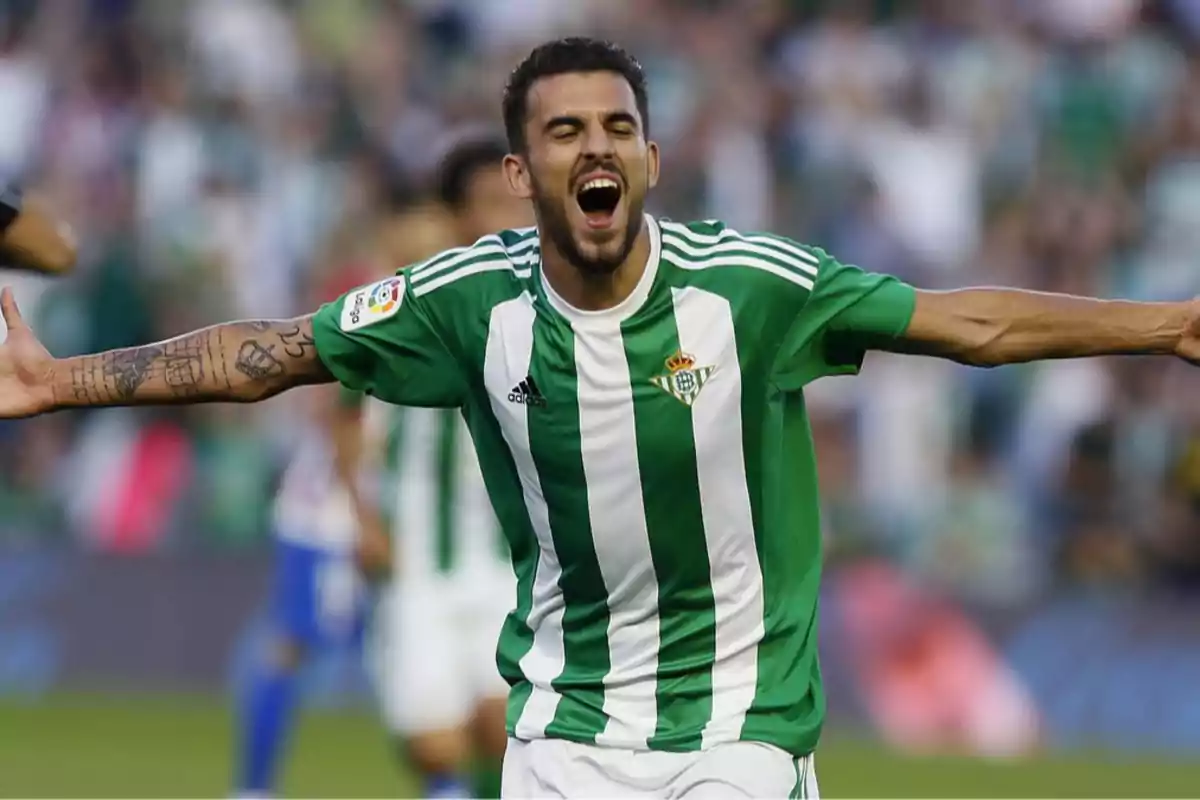 Futbolista celebrando un gol con los brazos abiertos vistiendo el uniforme verde y blanco del Real Betis en un estadio Futbolista celebrando un gol con los brazos abiertos vistiendo el uniforme verde y blanco del Real Betis en un estadio