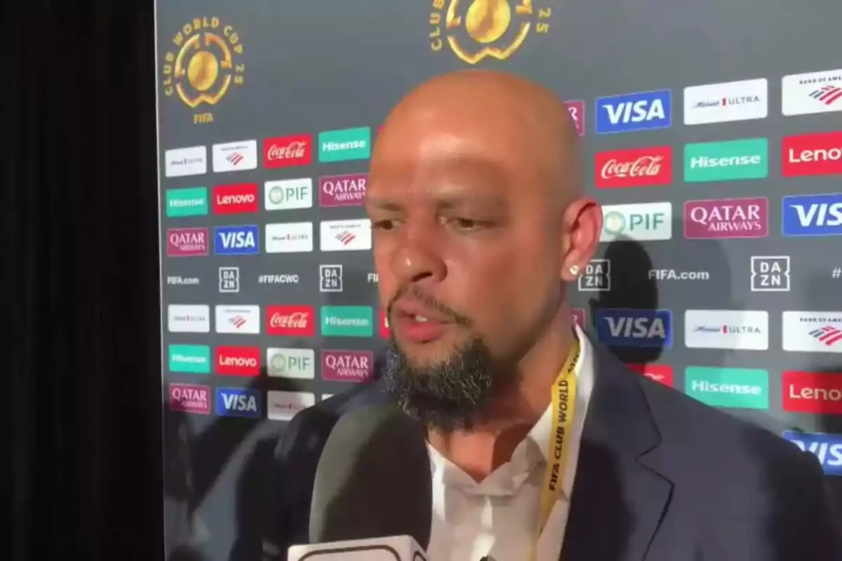 Bald man with a beard giving an interview in front of a backdrop with FIFA Club World Cup sponsor logos