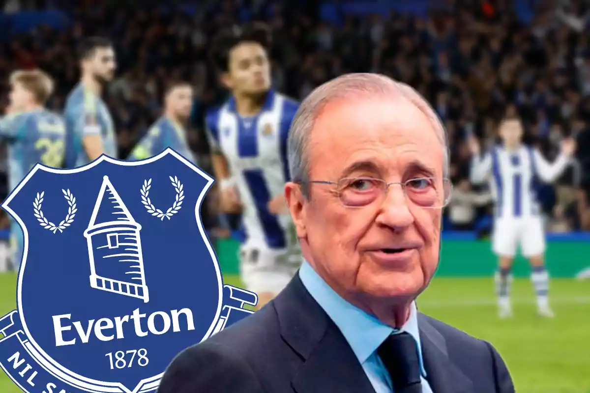 Older man with glasses and a suit in front of the Everton crest and blurred football players in the background